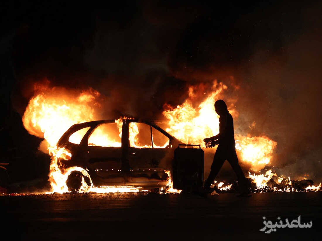 یک معترض فرانسوی از کنار یک اتومبیل در حال سوختن می گذرد