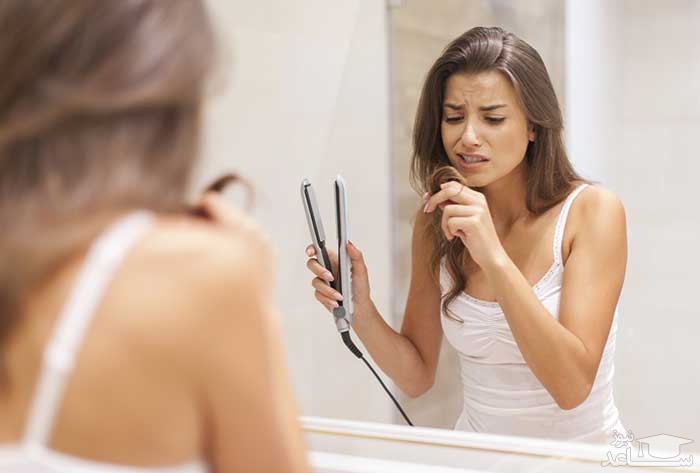 خانمی اتو مو به دست با ناراحتی به موهایش نگاه می کند.