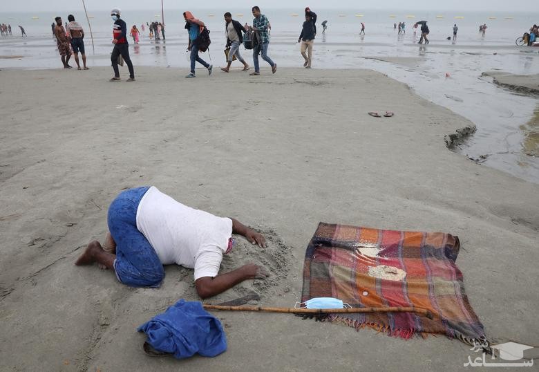 یک مرد در حاشیه جشنواره آیینی" ماکار سانکرانتی" هندوها برای دریافت صدقه از زائران در محل تلاقی رودخانه گنگ و خلیج بنگال سرش را داخل ماسه های ساحلی کرده است./ رویترز