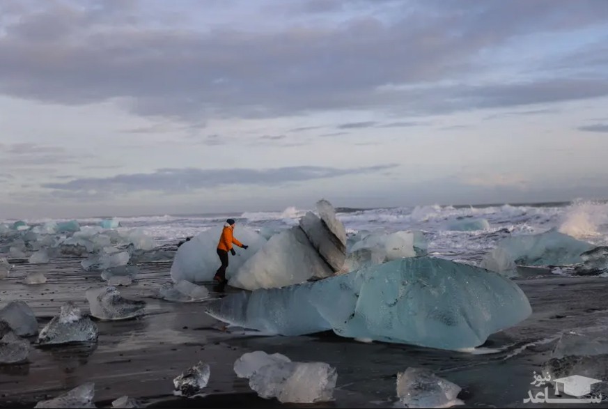 یک گردشگر در حال دست زدن به توده های یخی خرد شده در ایسلند/ رویترز