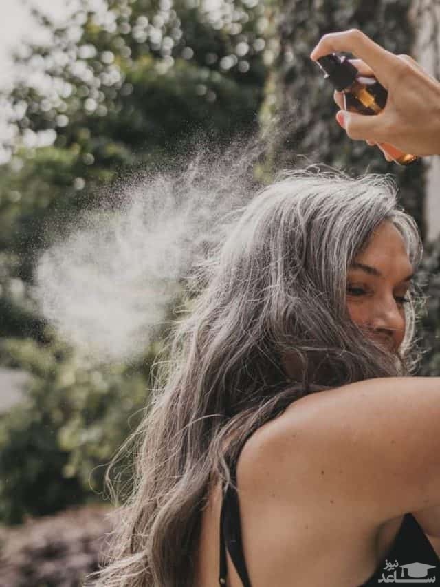 خانمی در حال اسپری کردن روی موهایش